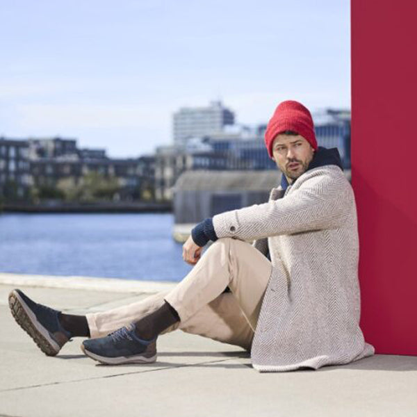 Man sitting by a waterfront with a red beanie and light coat